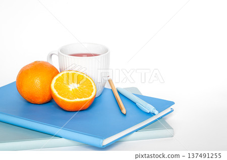 A cup of tea, orange and notebooks on a white background isolated, copy space. A cup of tea, orange and notebooks on a white background isolated, copy space. 137491255