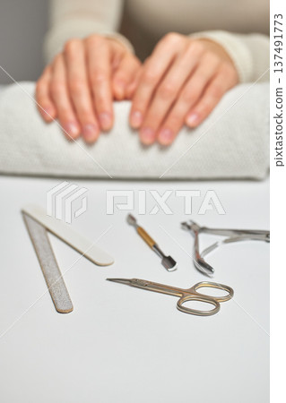 Woman's hands resting on a towel with various manicure tools on a white surface 137491773