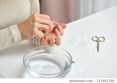Woman performing fingernail care with cuticle pusher and bowl of water Woman performing fingernail care with cuticle pusher and bowl of water 137491780