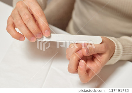 Woman performing a personal manicure at home, caring for her fingernails with a nail file 137491783