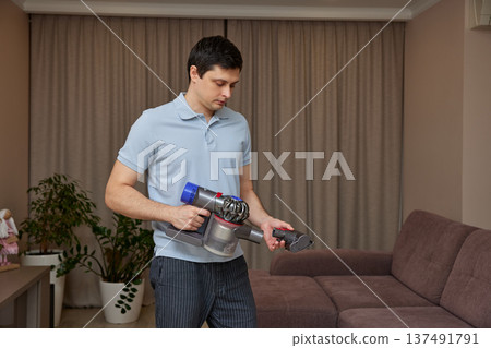 Man holding a modern cordless vacuum cleaner, preparing for housework Man holding a modern cordless vacuum cleaner, preparing for housework 137491791