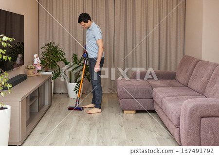 Man cleaning living room floor with a cordless vacuum cleaner 137491792