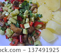 Close up of eggplant salad with cucumbers, tomatoes and fresh herbs served with boiled potatoes on a white plate 137491925