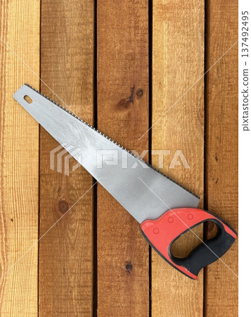 A hand saw with a metal handle lies on a stack of wooden boards 137492495