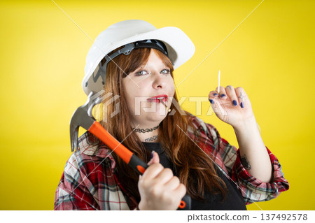 Woman wearing hard hat holding hammer and nail Woman wearing hard hat holding hammer and nail 137492578