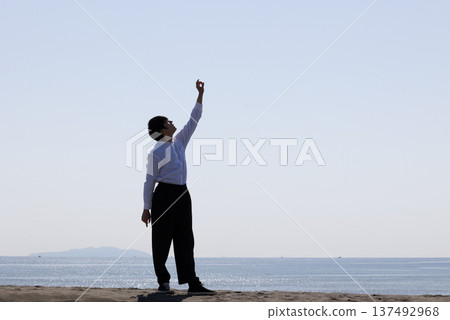 Silhouette of a man raising one hand towards the sky 137492968
