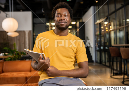 Male freelancer sitting casually on leather sofa holding notebook in coworking interior Male freelancer sitting casually on leather sofa holding notebook in coworking interior 137493596