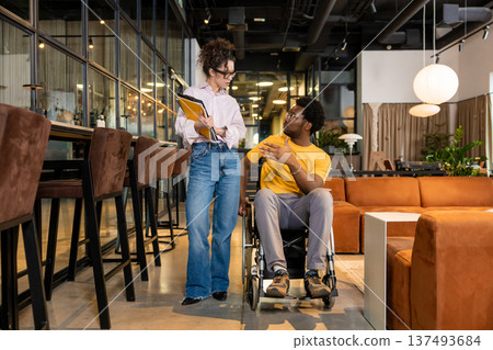 Businesswoman holding folders discussing with disabled man in shared workspace Businesswoman holding folders discussing with disabled man in shared workspace 137493684
