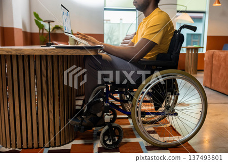 Man in wheelchair working on laptop with online business data in coworking space Man in wheelchair working on laptop with online business data in coworking space 137493801