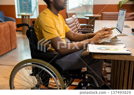 Man in wheelchair with coffee mug using laptop computer in coworking interior 137493829