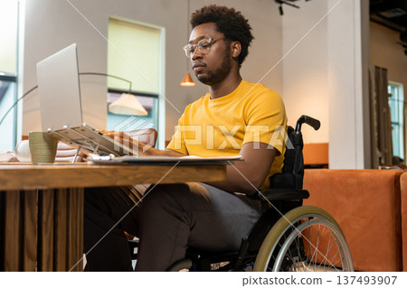 Man in wheelchair working on laptop with online business data in coworking space Man in wheelchair working on laptop with online business data in coworking space 137493907