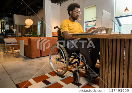 African American man in wheelchair concentrating on laptop African American man in wheelchair concentrating on laptop 137493909