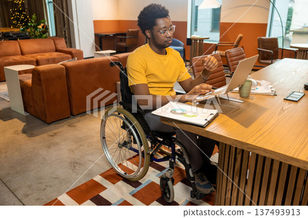 Serious disabled worker in wheelchair using laptop analyzing business data Serious disabled worker in wheelchair using laptop analyzing business data 137493913