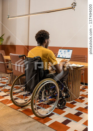 Man in wheelchair working attentively on laptop with migration analytics Man in wheelchair working attentively on laptop with migration analytics 137494000