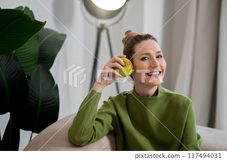 Young smiling woman in green with apple in hand Young smiling woman in green with apple in hand 137494031