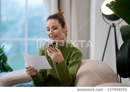 Woman in green blouse and jeans sitting on the sofa with a paper in hands 137494050