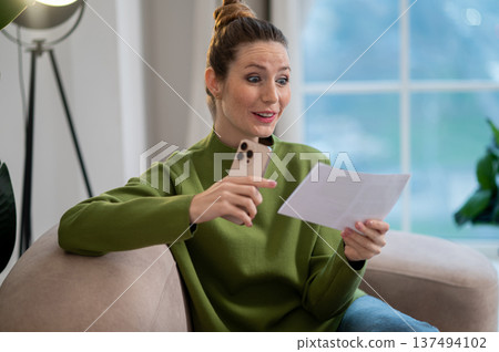 Woman in green blouse and jeans sitting on the sofa with a paper in hands 137494102