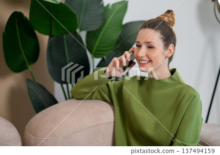 Woman in green sitting on the sofa and having a phone call 137494159