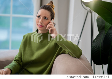 Woman in green sitting on the sofa and having a phone call 137494161