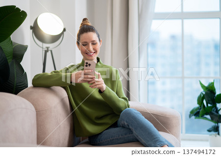 Woman in green sitting on the sofa and having a phone call 137494172