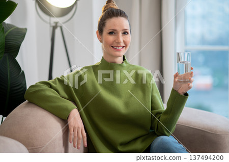 Pretty young woman in green sitting on the sofa with a glass of water 137494200