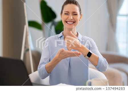 Smiling cute young woman explaining something on video call by sign language Smiling cute young woman explaining something on video call by sign language 137494283
