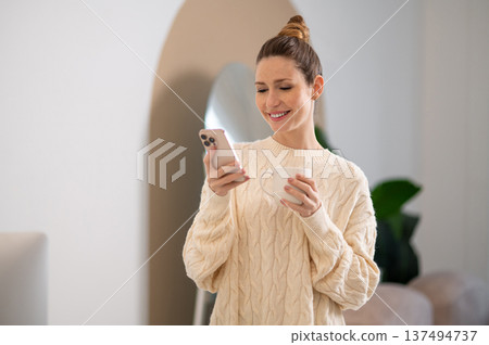 Cute caucasian woman in white sweater with a cup in hands Cute caucasian woman in white sweater with a cup in hands 137494737