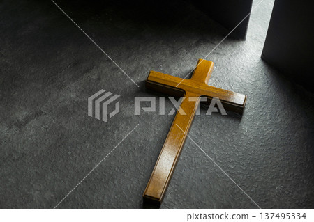 Simple wooden Christian cross on a dark textured surface, dramatically illuminated by a bright shaft of light from a doorway, symbolizing faith, hope, and spiritual light in the darkness Simple wooden Christian cross on a dark textured surface, dramatically illuminated by a bright shaft of light from a doorway, symbolizing faith, hope, and spiritual light in the darkness 137495334