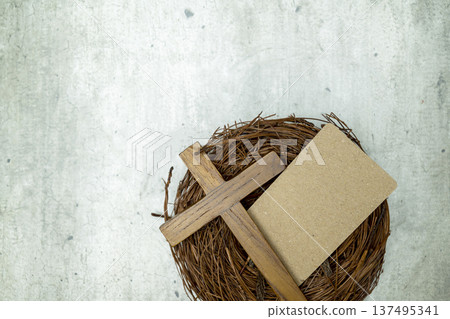 A wooden Christian cross and blank craft paper card in a twig nest on a grey textured surface, suitable for religious themes, Easter greetings, or sympathy cards 137495341