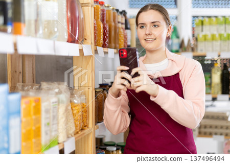 Girl merchandiser photographs shelves with goods and creates photo report of rearrange work result 137496494