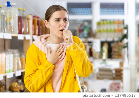 Woman in windbreaker coughing in store Woman in windbreaker coughing in store 137496512