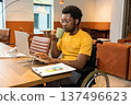 Man in wheelchair with coffee mug using laptop computer in coworking interior 137496623
