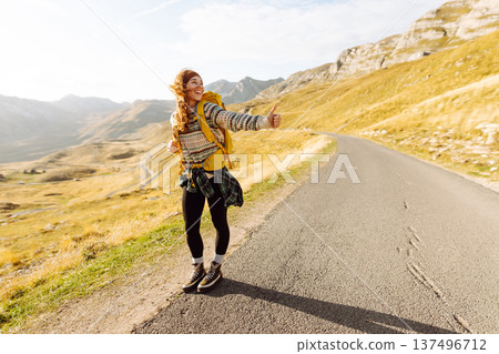 Hitchhiking woman traveler try to stop car on the mountain road. Travel and vacation theme 137496712