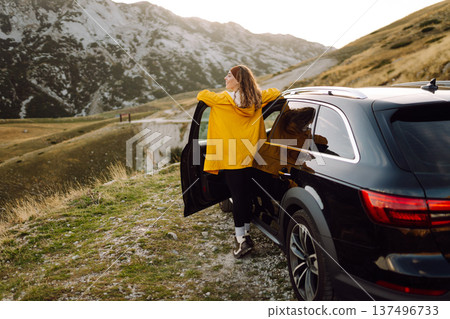 A cheerful traveler enjoying a scenic mountain view while sitting on the trunk. Travelling by car. A cheerful traveler enjoying a scenic mountain view while sitting on the trunk. Travelling by car. 137496733