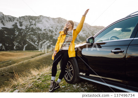 A cheerful traveler enjoying a scenic mountain view while sitting on the trunk. Travelling by car. A cheerful traveler enjoying a scenic mountain view while sitting on the trunk. Travelling by car. 137496734