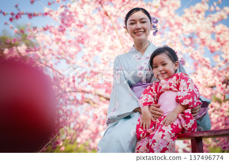 woman and child girl in yukata (kimono dress) on red bridge with sakura flower or cherry blossom blooming in garden 137496774