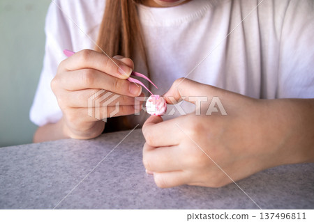 Young girl delicately decorating a tiny pink cupcake with tweezers, focused creativity and gentle concentration Young girl delicately decorating a tiny pink cupcake with tweezers, focused creativity and gentle concentration 137496811
