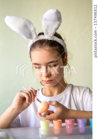 Girl wearing bunny ears painting a pastel Easter egg with focused care and creative concentration at home Girl wearing bunny ears painting a pastel Easter egg with focused care and creative concentration at home 137496812