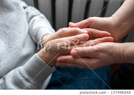 Caregiver holding elderly person's hands in a gentle act of support and compassion at home Caregiver holding elderly person's hands in a gentle act of support and compassion at home 137496848