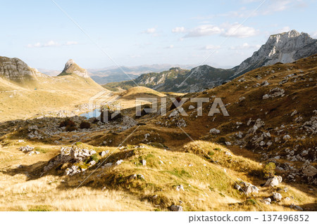 Golden sunlight illuminates vast mountain landscape with rolling hills and rocky outcrops in sunset Golden sunlight illuminates vast mountain landscape with rolling hills and rocky outcrops in sunset 137496852