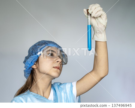 Young scientist in protective gear examining a blue solution in a test tube during research 137496945