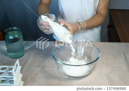 Close-up of gloved hands pouring a white substance into a glass bowl. Close-up of gloved hands pouring a white substance into a glass bowl. 137496990