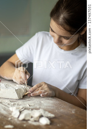 Young artist carving clay sculpture at a bright studio table with focus and patience 137497031