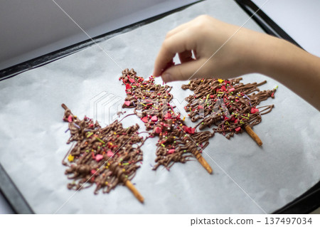 Chocolate drizzle pretzel sticks with colorful sprinkles on a baking tray, hand decorating a festive treat 137497034