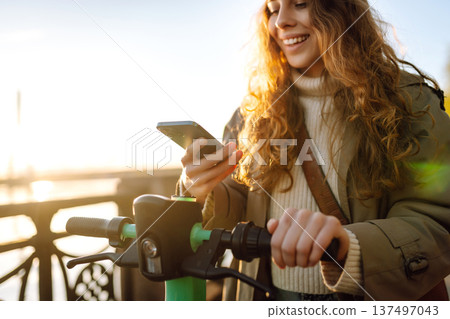 Woman driving electric scooter through city. Ecological transportation. Travel, tourism concept. Woman driving electric scooter through city. Ecological transportation. Travel, tourism concept. 137497043