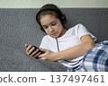 Girl with headphones relaxing on couch using mobile phone in casual home setting 137497461