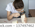 Girl examines wooden block with magnifying glass during a wood craft project at a desk 137497462