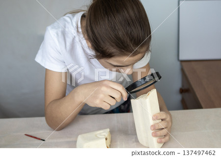 Girl examines wooden block with magnifying glass during a wood craft project at a desk 137497462