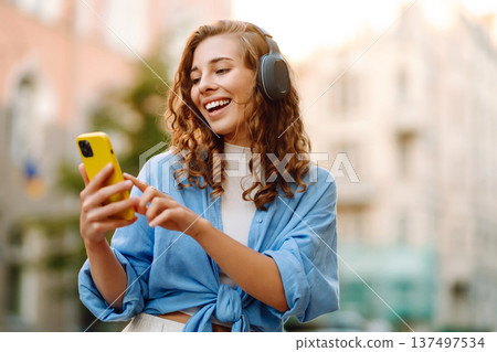 Happy relaxed woman in wireless headphones choosing, listening favorite music in urban city street. Happy relaxed woman in wireless headphones choosing, listening favorite music in urban city street. 137497534