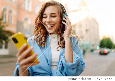 Happy relaxed woman in wireless headphones choosing, listening favorite music in urban city street. 137497537